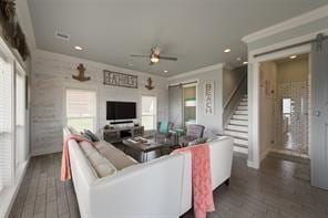 living room with dark wood-type flooring, ornamental molding, a barn door, and ceiling fan