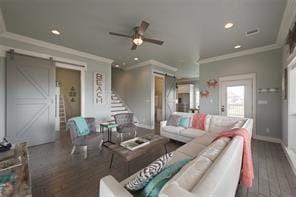 living room with dark wood-type flooring, ceiling fan, a barn door, and crown molding