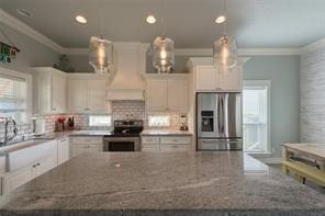 kitchen featuring crown molding, premium range hood, white cabinetry, stainless steel appliances, and dark stone counters