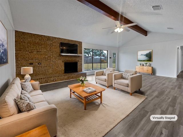 living room with ceiling fan, hardwood / wood-style floors, a fireplace, lofted ceiling with beams, and a textured ceiling