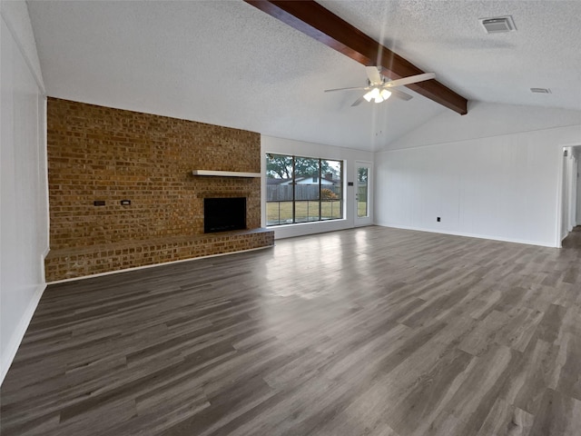 unfurnished living room with dark wood-type flooring, lofted ceiling with beams, a brick fireplace, a textured ceiling, and ceiling fan