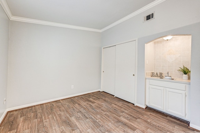 unfurnished bedroom with ornamental molding, sink, light hardwood / wood-style floors, and a closet