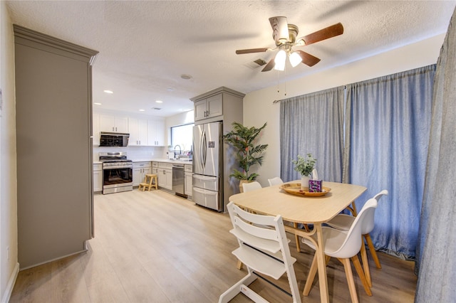 dining room featuring ceiling fan, sink, light hardwood / wood-style floors, and a textured ceiling