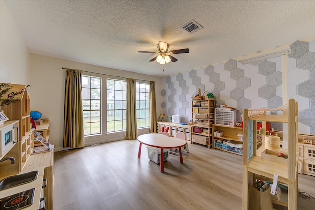 recreation room with ceiling fan, light hardwood / wood-style floors, and a textured ceiling