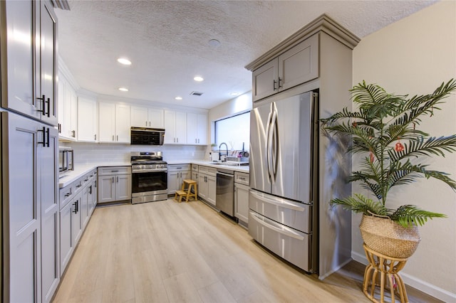 kitchen featuring sink, gray cabinetry, tasteful backsplash, light wood-type flooring, and stainless steel appliances