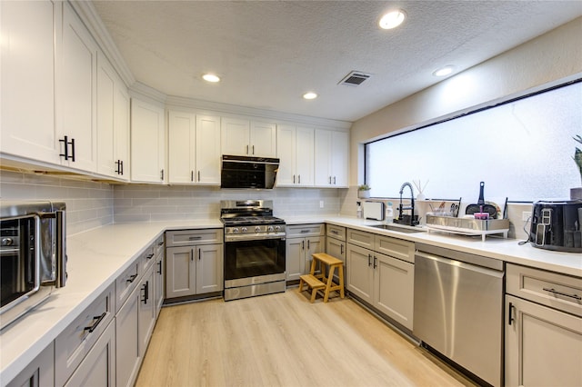 kitchen with appliances with stainless steel finishes, sink, backsplash, a textured ceiling, and light hardwood / wood-style flooring