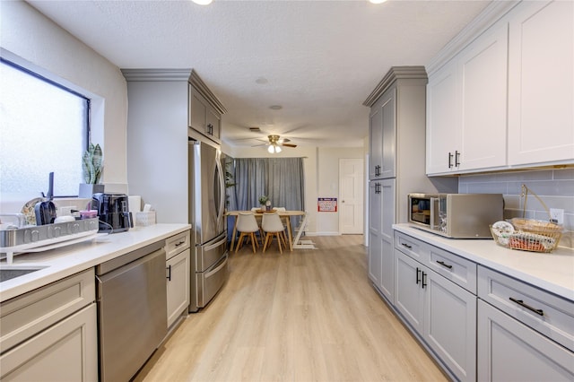 kitchen featuring light hardwood / wood-style flooring, ceiling fan, appliances with stainless steel finishes, gray cabinetry, and decorative backsplash