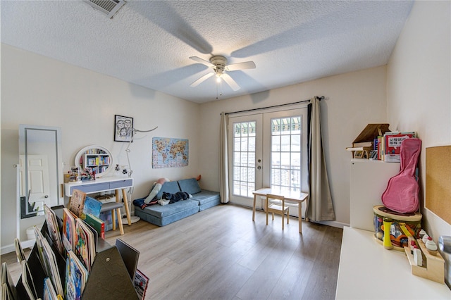 game room with french doors, ceiling fan, light hardwood / wood-style floors, and a textured ceiling