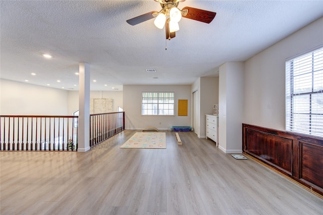 unfurnished room with ceiling fan, a healthy amount of sunlight, a textured ceiling, and light wood-type flooring