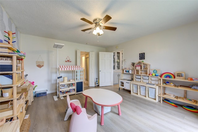 rec room featuring ceiling fan, light hardwood / wood-style flooring, and a textured ceiling