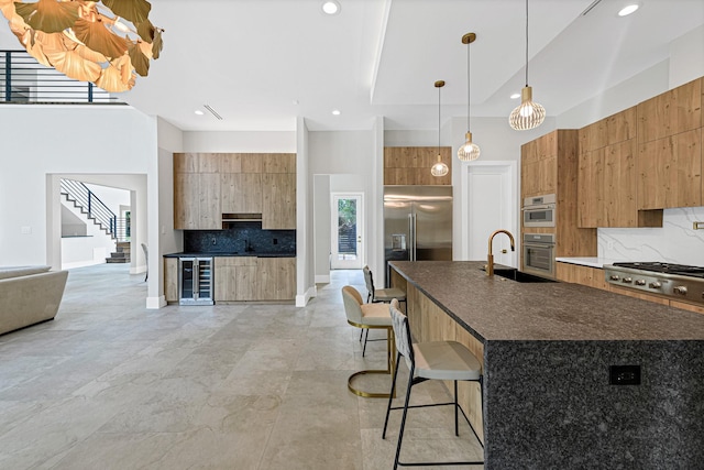 kitchen with decorative light fixtures, an island with sink, sink, wine cooler, and a kitchen bar