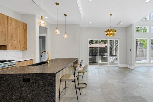 kitchen featuring sink, tasteful backsplash, hanging light fixtures, a kitchen breakfast bar, and a kitchen island with sink