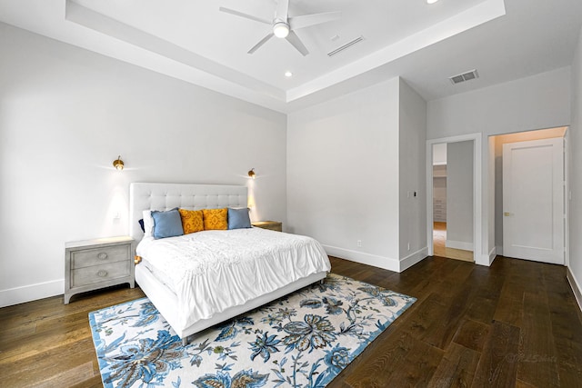 bedroom with dark hardwood / wood-style flooring, a tray ceiling, and ceiling fan