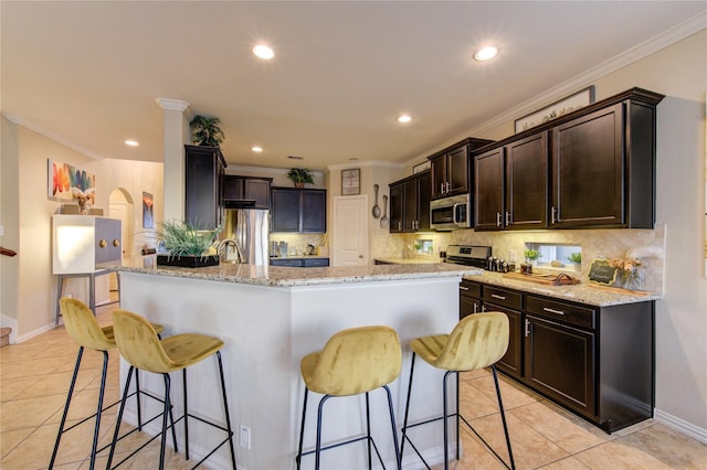 kitchen featuring light tile patterned flooring, a kitchen bar, light stone counters, ornamental molding, and appliances with stainless steel finishes