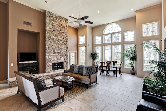 tiled living room featuring a stone fireplace, ornamental molding, ceiling fan, and a high ceiling