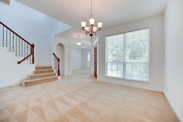 foyer entrance with a healthy amount of sunlight, light colored carpet, and a notable chandelier