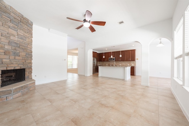 unfurnished living room featuring a stone fireplace and ceiling fan