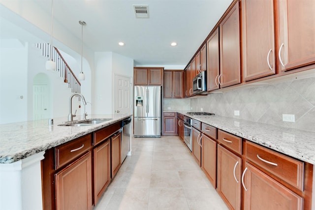 kitchen with hanging light fixtures, appliances with stainless steel finishes, sink, and light stone counters