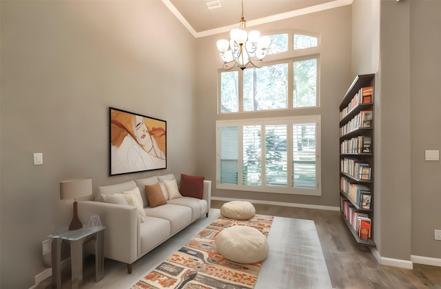 living area with an inviting chandelier, crown molding, hardwood / wood-style flooring, and a high ceiling