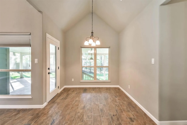 unfurnished dining area with hardwood / wood-style floors, a notable chandelier, and vaulted ceiling