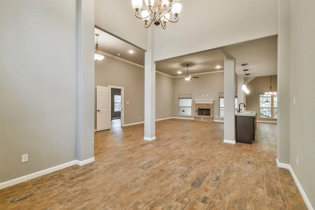 unfurnished living room featuring a stone fireplace, sink, light hardwood / wood-style flooring, ornamental molding, and ceiling fan with notable chandelier