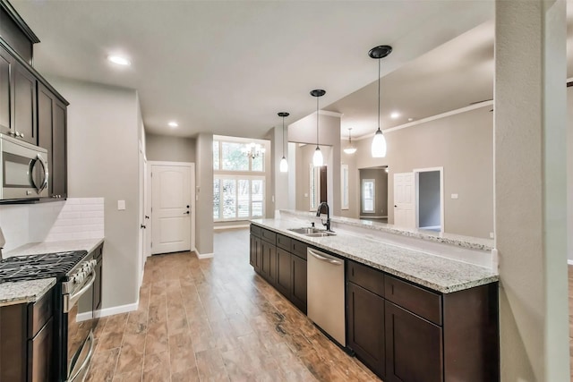 kitchen featuring appliances with stainless steel finishes, sink, hanging light fixtures, light stone countertops, and dark brown cabinets