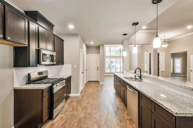 kitchen with decorative light fixtures, sink, stainless steel appliances, light stone countertops, and dark brown cabinets