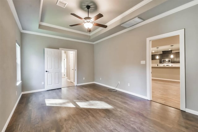 empty room featuring crown molding, ceiling fan, dark hardwood / wood-style flooring, and a raised ceiling