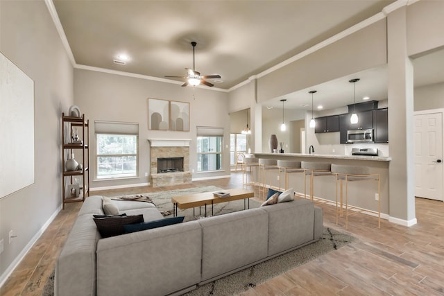 living room with crown molding, hardwood / wood-style flooring, ceiling fan, a high ceiling, and a fireplace