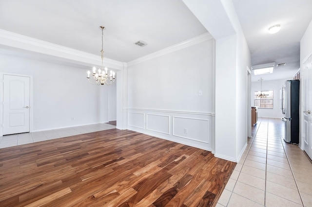 unfurnished dining area featuring crown molding, light hardwood / wood-style floors, and a notable chandelier