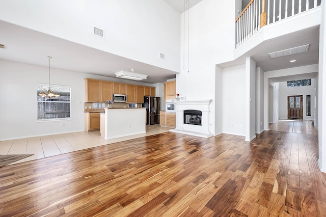 unfurnished living room with a high ceiling, a notable chandelier, and light wood-type flooring