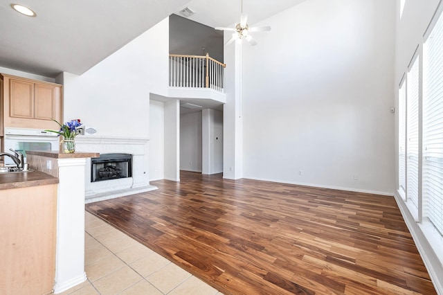 unfurnished living room featuring sink, light hardwood / wood-style floors, ceiling fan, and a high ceiling