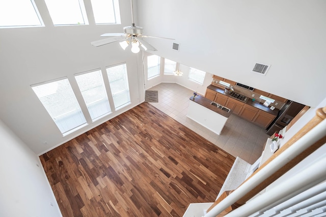 unfurnished living room with ceiling fan, a towering ceiling, dark hardwood / wood-style flooring, and sink