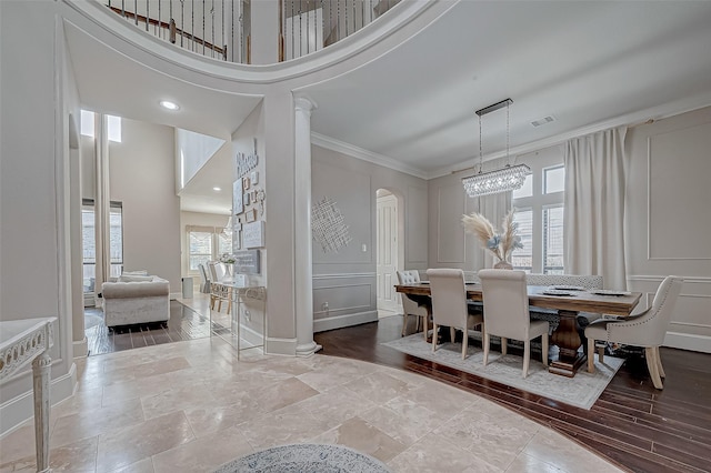 dining space featuring light hardwood / wood-style flooring, ornamental molding, a notable chandelier, decorative columns, and a high ceiling