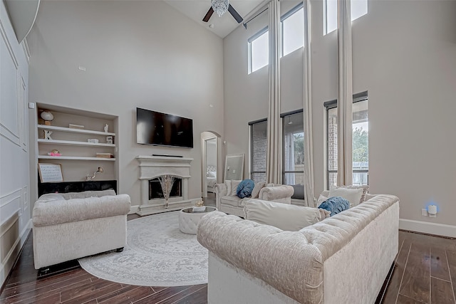 living room with ceiling fan, dark hardwood / wood-style floors, high vaulted ceiling, and built in features