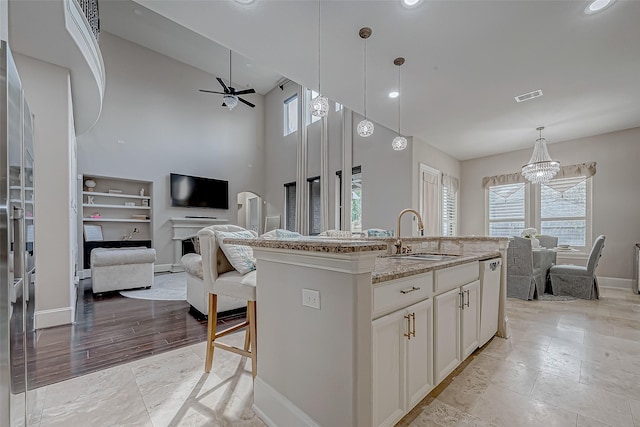 kitchen with sink, white cabinetry, pendant lighting, light stone countertops, and a kitchen island with sink