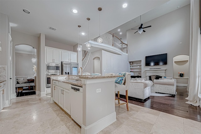 kitchen featuring an island with sink, pendant lighting, stainless steel appliances, light stone countertops, and white cabinets