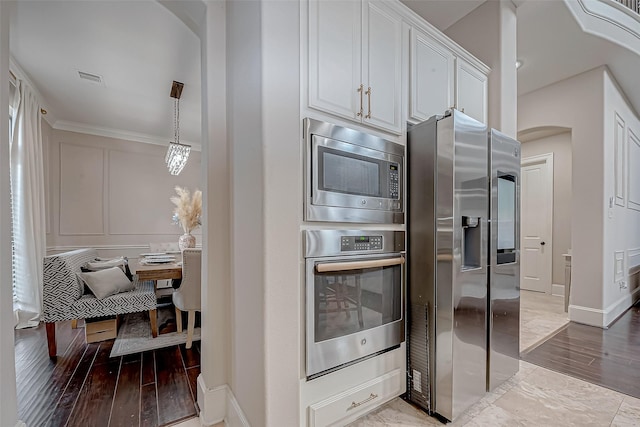 kitchen with decorative light fixtures, ornamental molding, appliances with stainless steel finishes, hardwood / wood-style flooring, and white cabinets