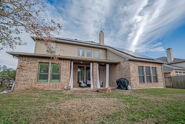 rear view of property featuring a patio, a lawn, and solar panels