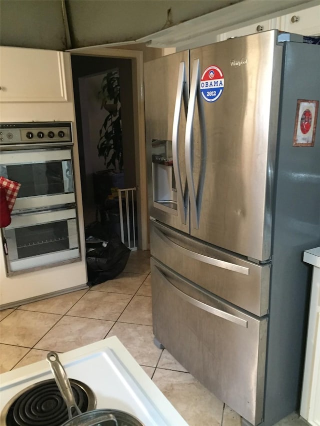 kitchen with stainless steel appliances, light tile patterned floors, and white cabinets