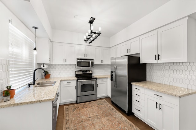 kitchen with sink, appliances with stainless steel finishes, white cabinetry, light stone counters, and decorative light fixtures