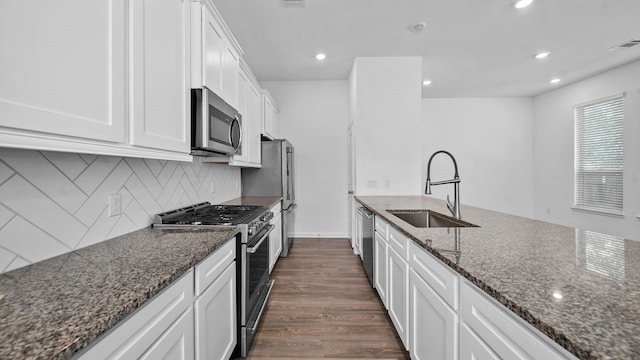 kitchen with appliances with stainless steel finishes, sink, dark stone countertops, white cabinets, and dark hardwood / wood-style flooring