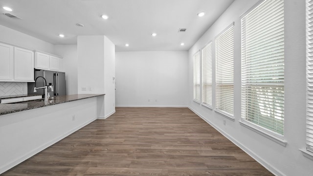 kitchen with high end fridge, white cabinetry, dark hardwood / wood-style floors, dark stone counters, and backsplash