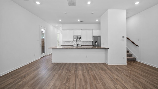 kitchen with appliances with stainless steel finishes, white cabinets, dark hardwood / wood-style flooring, decorative backsplash, and dark stone counters