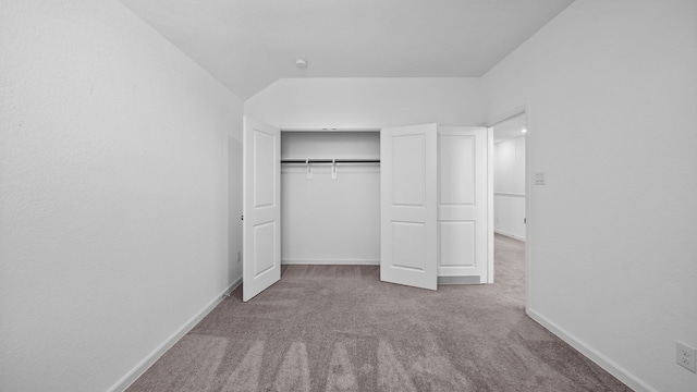 unfurnished bedroom with light colored carpet, lofted ceiling, and a closet