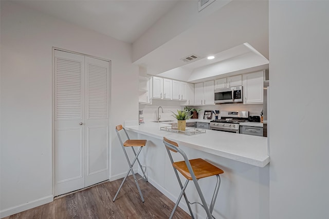 kitchen featuring sink, appliances with stainless steel finishes, white cabinetry, a kitchen breakfast bar, and kitchen peninsula