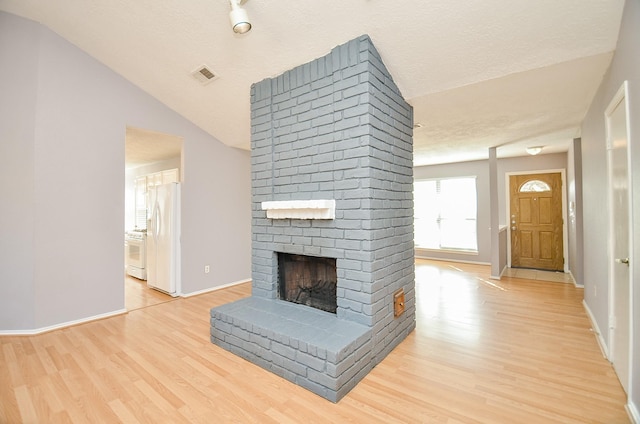 unfurnished living room featuring lofted ceiling, a textured ceiling, a fireplace, and light hardwood / wood-style flooring