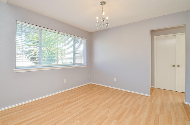 spare room with a chandelier and light wood-type flooring