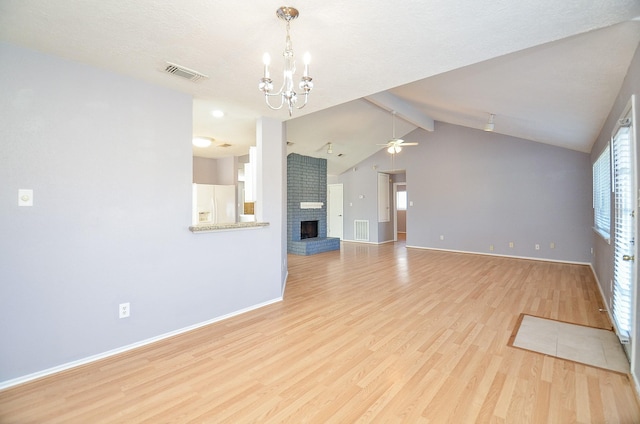 unfurnished living room featuring ceiling fan with notable chandelier, lofted ceiling with beams, a brick fireplace, and light hardwood / wood-style flooring