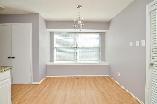 unfurnished dining area with a textured ceiling, light hardwood / wood-style floors, and a chandelier